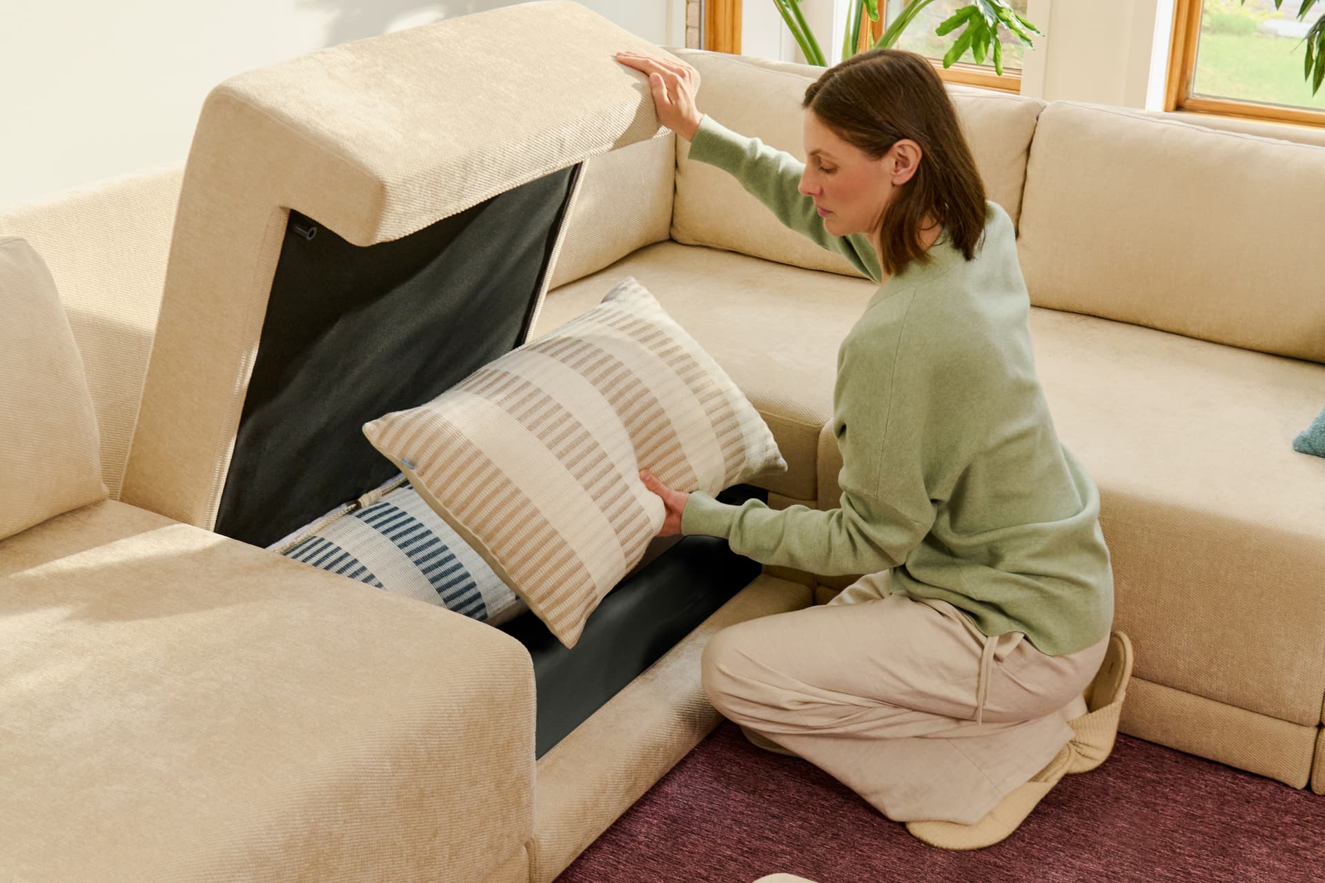 Woman placing a pillow into the hidden storage compartment of a cream Cozey sofa