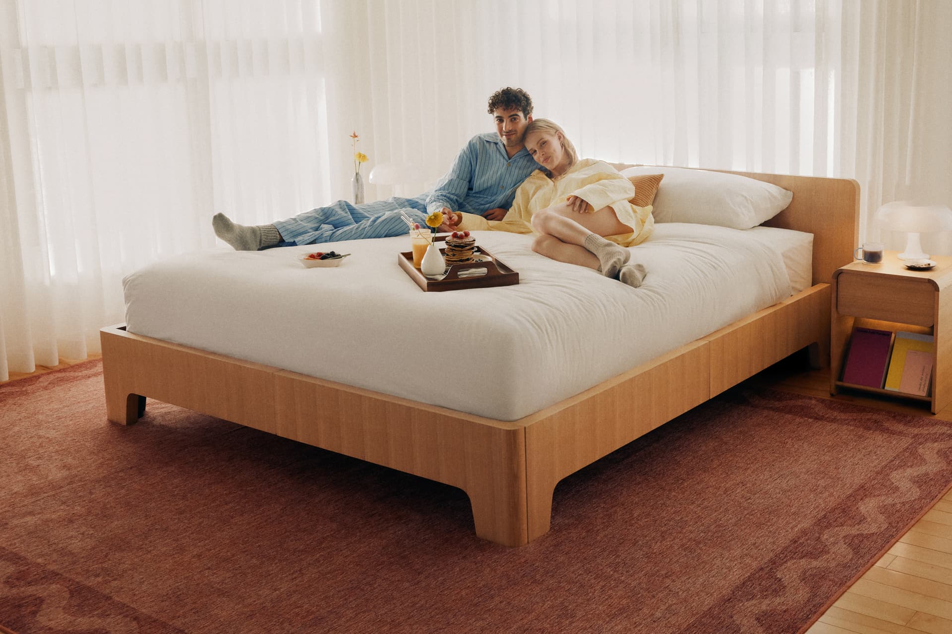 A couple relaxing with breakfast on a Cozey Ara bed with a light wood frame